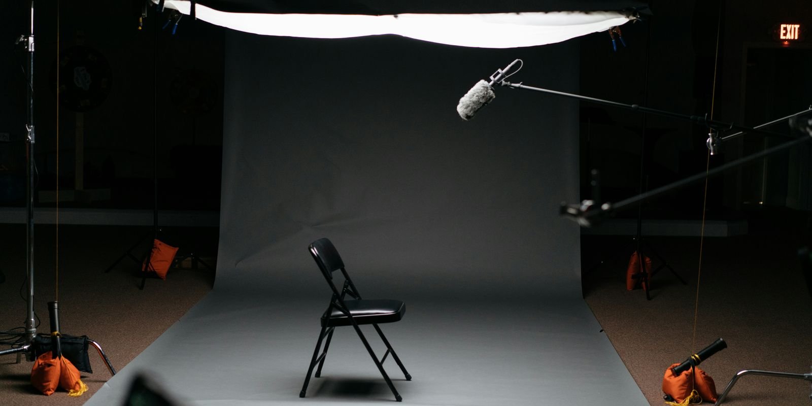 A film set: a lone chair under an overhead light, crew kit in the dark