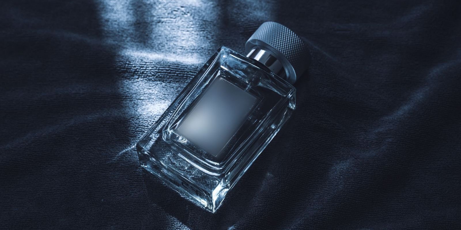 Product study: a glass perfume bottle on dark fabric under a single key light