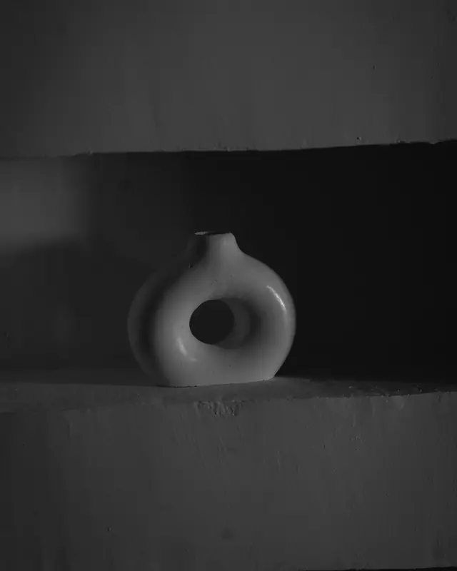 A ring-shaped ceramic vase on a concrete shelf