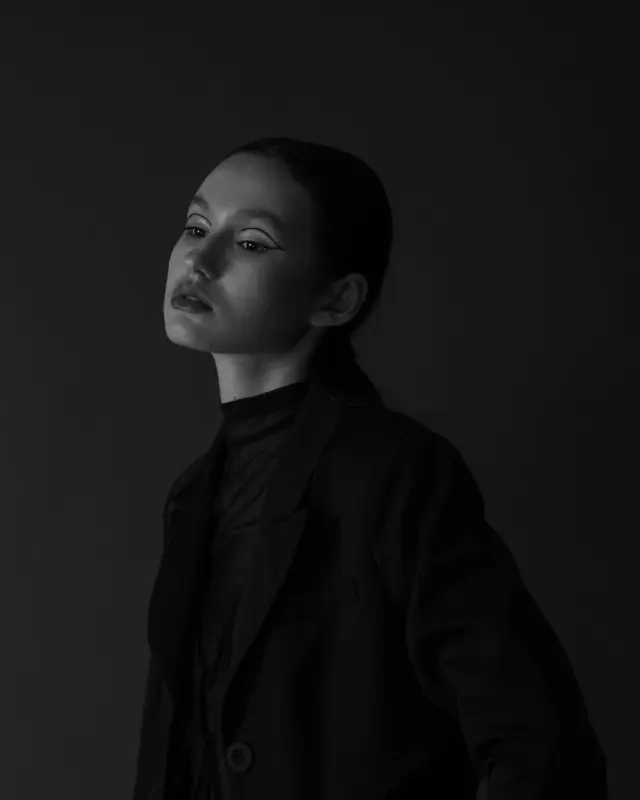 A black-and-white studio portrait in a long coat