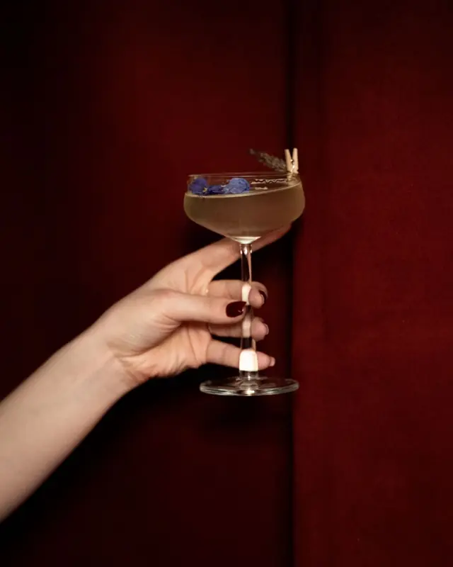 A hand holding a cocktail against a red curtain