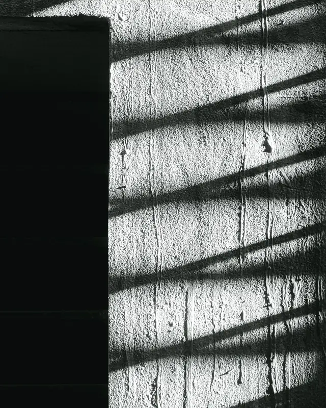 Striped shadows across a textured concrete wall